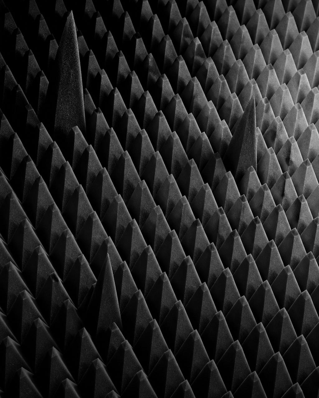 Macro grayscale image of anechoic foam where a few tall wedges are smoothed toward uniform height, a metaphor for per-submodule outlier smoothing.